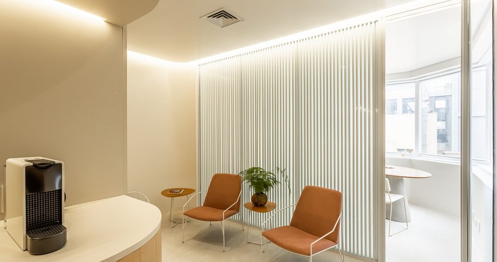 Máquina de café no balcão da recepção, com as poltronas da espera ao fundo