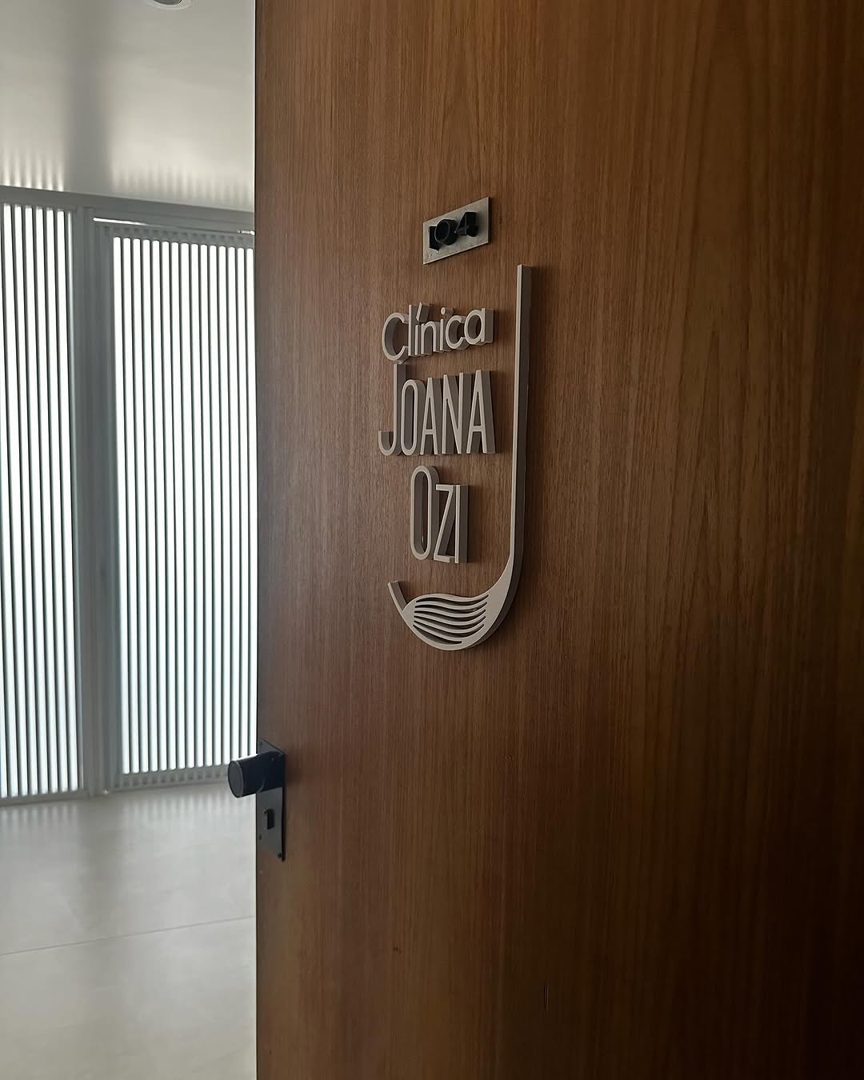 Porta de madeira com a placa da Clínica Joana Ozi na entrada do consultório