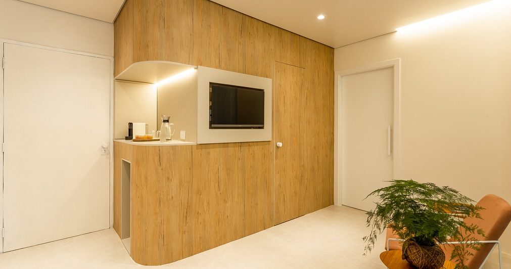 Recepção da clínica com painel de madeira, TV e planta